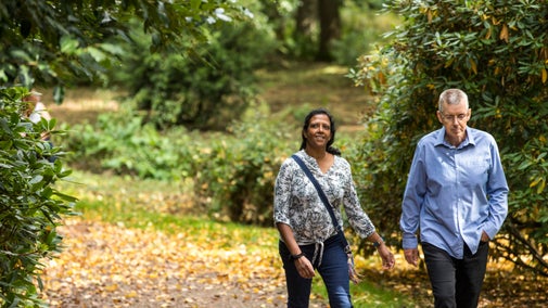 Couple walking along pathway lined with autumn leaves at Attingham Park